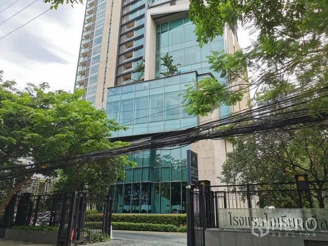 Condominium for rent in Pathum Wan, Bangkok - Secure gated entrance of the condominium framed by mature trees.