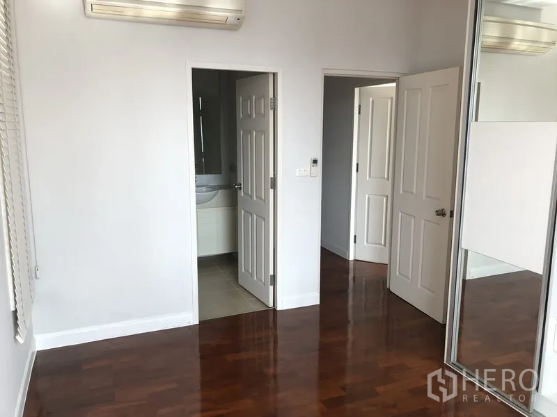 Condominium for rent in Khlong Toei, Bangkok - Corner bedroom with mirrored sliding closet doors and access to an ensuite bathroom.