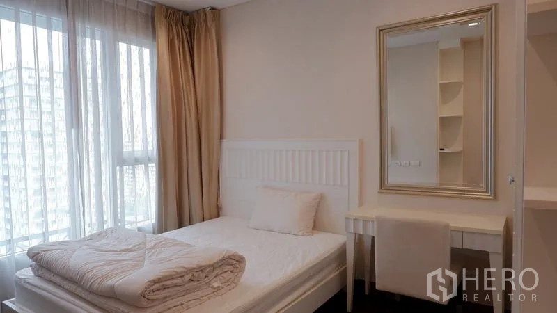 Condominium for rent in Watthana, Bangkok - Bright bedroom with vanity desk, mirror, and sheer curtains.