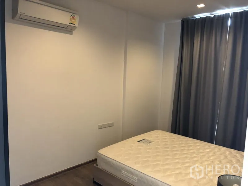 Condominium for rent in Watthana, Bangkok - Second bedroom featuring a bed, blackout curtains, and wall‑mounted air conditioner.