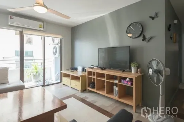 公寓 出租在Watthana, Bangkok - 客厅配电视柜、灰色特色墙、吊扇，推拉玻璃门通往阳台。