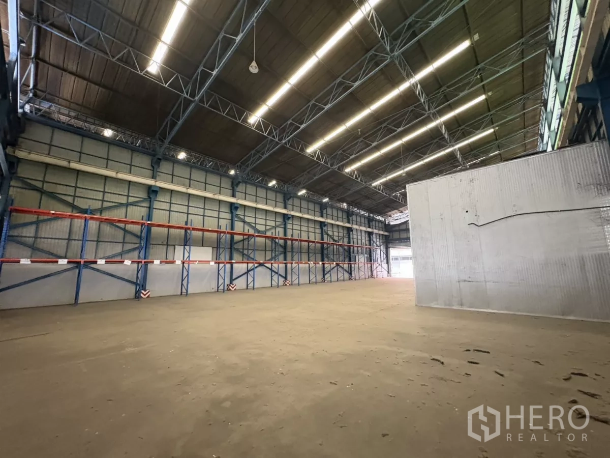 Warehouse for rent in Mueang Samut Prakan, Samut Prakan - Wide clear floor under a steel truss roof with long racking along the wall.