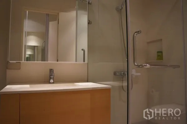 Condominium for rent in Ratchathewi, Bangkok - Contemporary bathroom featuring glass-enclosed shower and wide vanity with mirror.