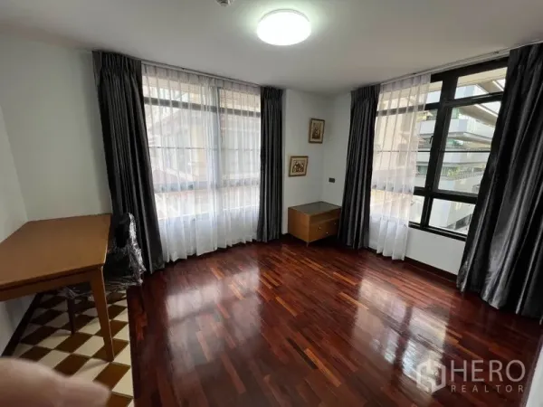 Condominium for rent or sale in Watthana, Bangkok - Bright corner room with large windows, sheer curtains, polished wood floor and study desk.