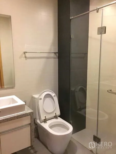 Condominium for sale in Khlong Toei, Bangkok - Guest bathroom with glass shower, toilet and vanity on tiled floors.