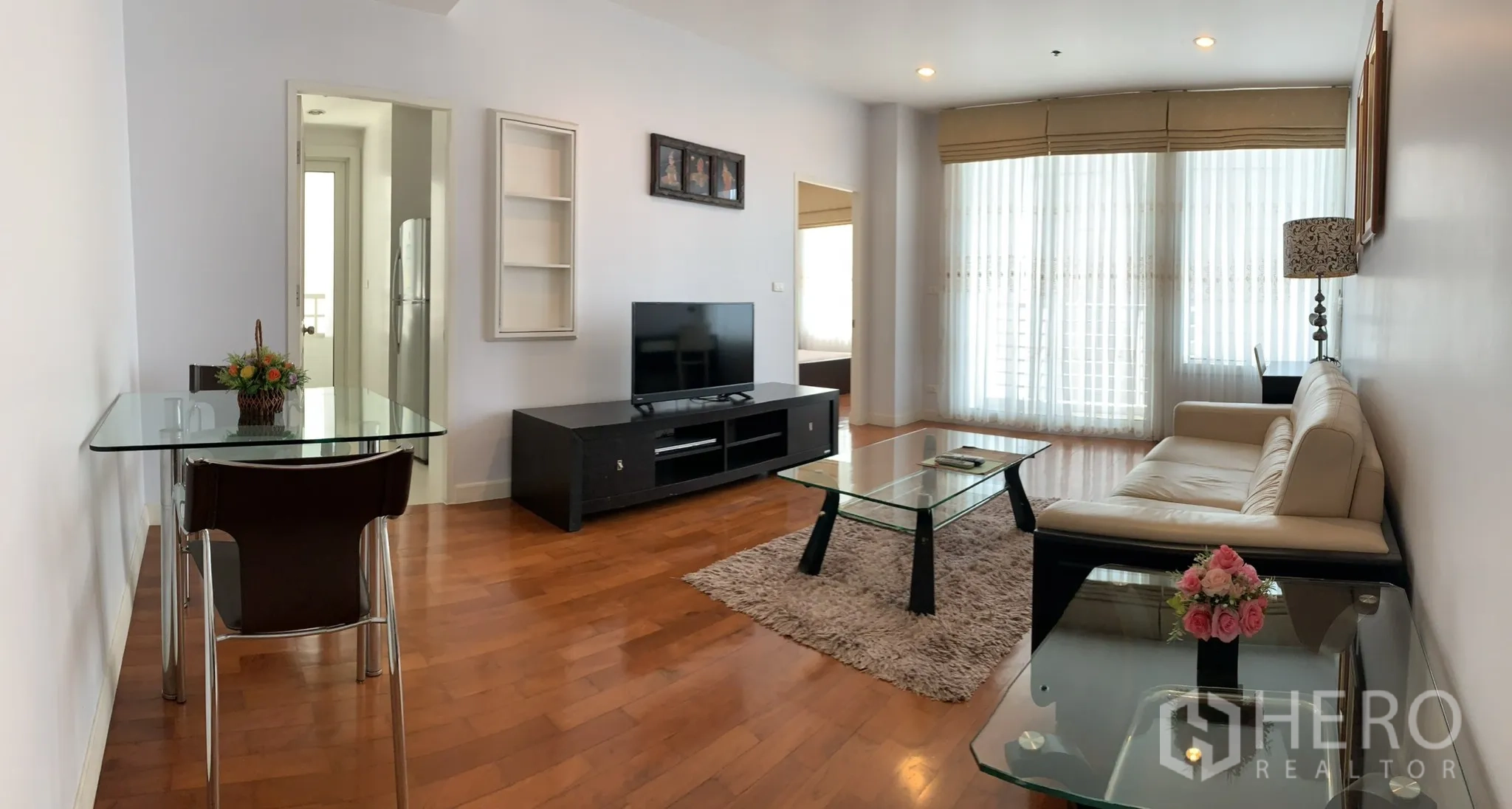 Condominium for rent in Khlong Toei, Bangkok - Open-plan living and dining area with glass tables, TV cabinet and sheer curtains filling the space with natural light.