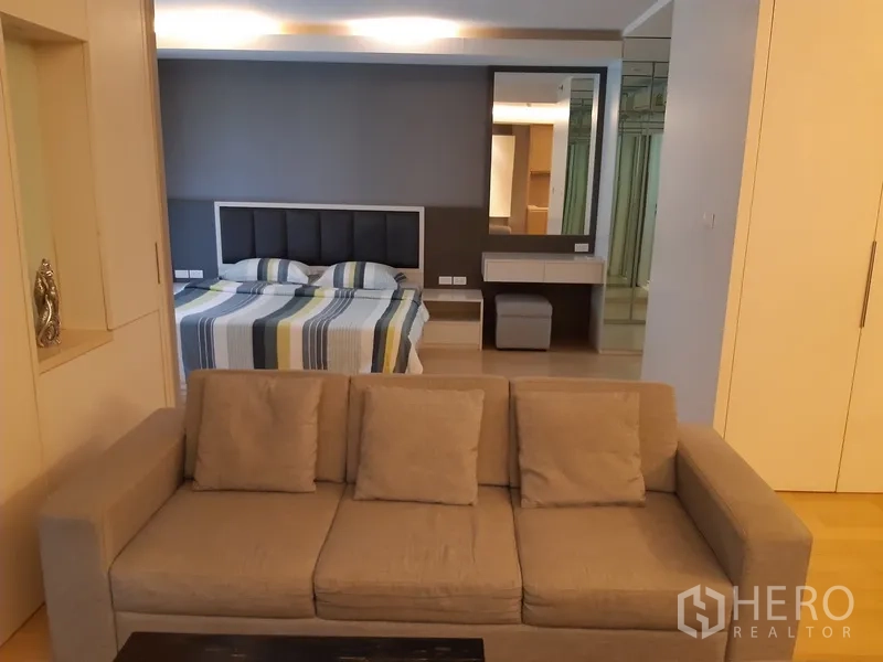 公寓 出租在Watthana, Bangkok - 开放式布局，前景为沙发，后方可见卧室与梳妆区。