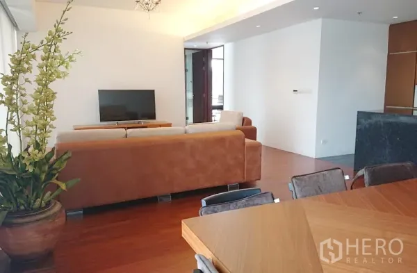 Condominium for sale in Pathum Wan, Bangkok - Bright living area with chandelier, large potted plant, TV console and dining set by the windows.