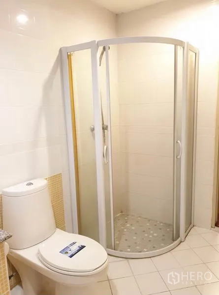 Townhouse for rent or sale in Chatuchak, Bangkok - Bathroom with curved glass shower enclosure and toilet in a white-tiled interior.