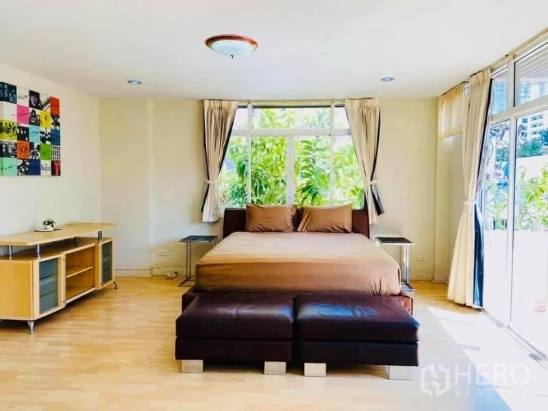 Detached House for rent in Watthana, Bangkok - Spacious bedroom with king bed, ottomans and full-height windows facing the garden.
