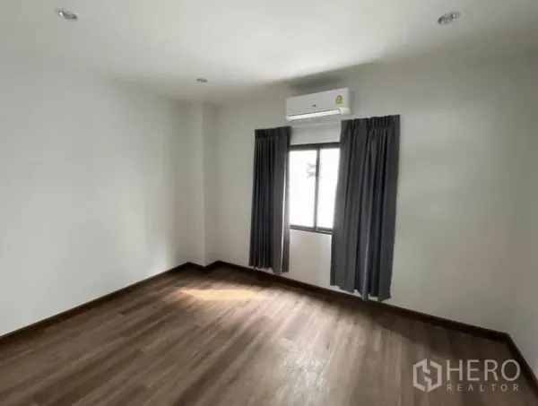 Townhouse for rent in Bang Na, Bangkok - Air-conditioned bedroom with wood flooring, white walls and a curtained window.