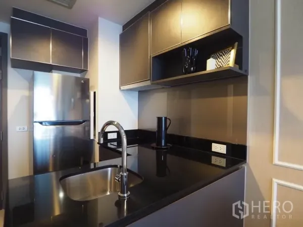 Condominium for rent in Khlong San, Bangkok - Modern kitchenette featuring stainless refrigerator, black granite worktop, and sink.