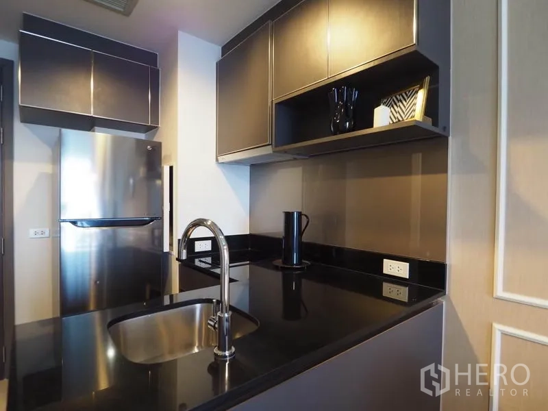 Condominium for rent in Khlong San, Bangkok - Modern kitchenette featuring stainless refrigerator, black granite worktop, and sink.
