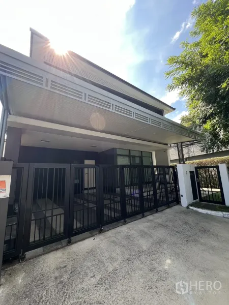Detached House for sale in Bang Kapi, Bangkok - Modern two-storey corner house with black sliding gate and sun flare.