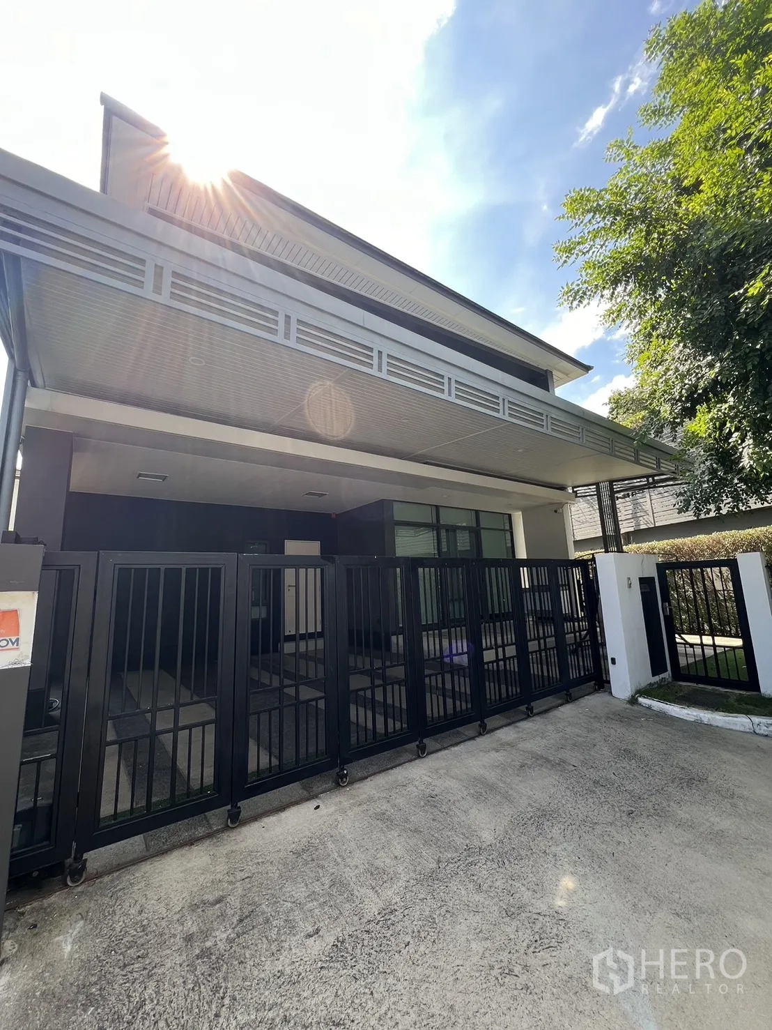 Detached House for sale in Bang Kapi, Bangkok - Modern two-storey corner house with black sliding gate and sun flare.
