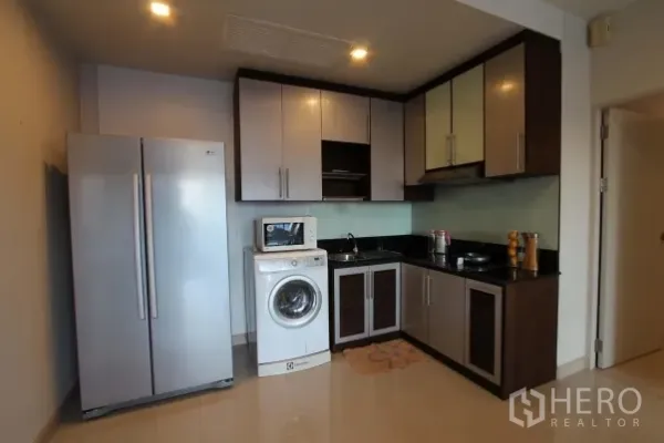 Condominium for rent in Watthana, Bangkok - Compact kitchen with stainless double‑door fridge, washing machine, microwave and upper cabinets.