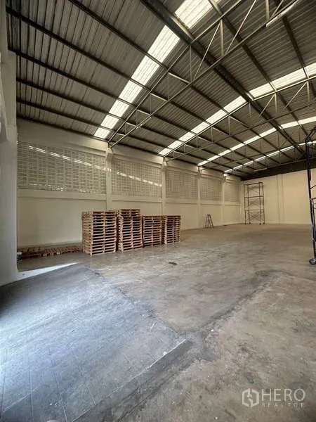 Warehouse for rent in Suan Luang, Bangkok - Warehouse space with stacked wooden pallets, smooth concrete floor, and airy metal roof.