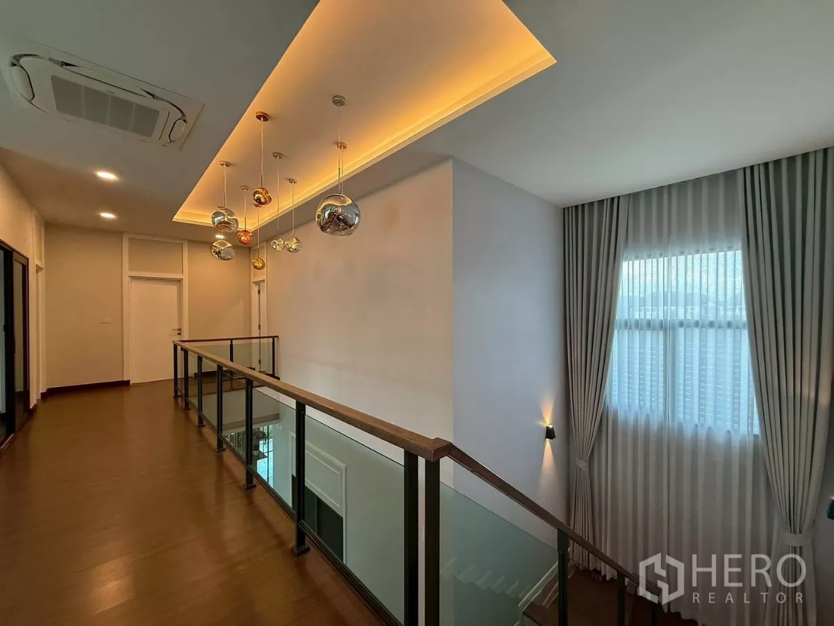 独立式住宅 出租在Bang Phli, Samut Prakan - 二楼走廊，玻璃栏杆、暖色灯槽和纱帘。