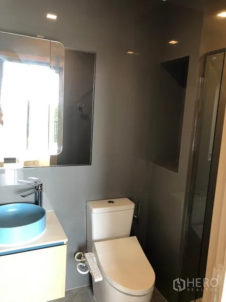 Condominium for rent in Watthana, Bangkok - Sleek bathroom featuring blue vessel sink, mirror, toilet and glass shower.