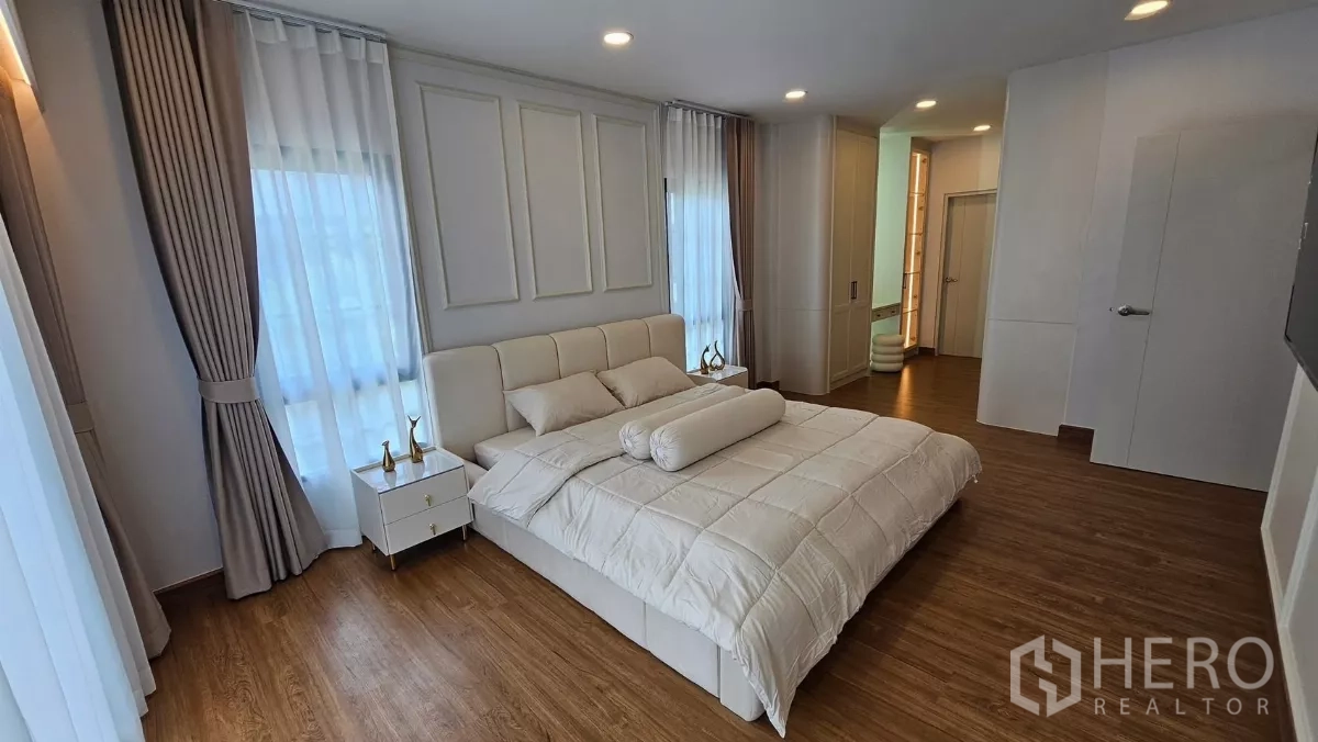 独立式住宅 出租或出售在Bang Phli, Samut Prakan - 主卧宽敞，配特大床、木地板、多面窗及通往套卫与衣帽间的入口。