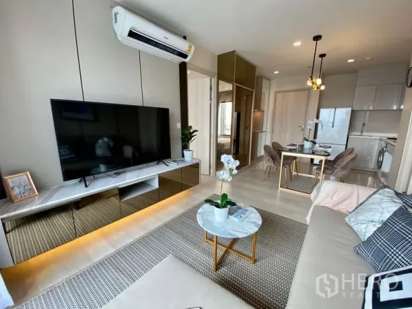 คอนโด ให้เช่าในPathum Wan, Bangkok - มุมห้องรับแขกแบบเปิดโล่ง มีทีวี พรม และมองต่อเนื่องไปยังโซนรับประทานอาหารกับครัวขนาดกะทัดรัด