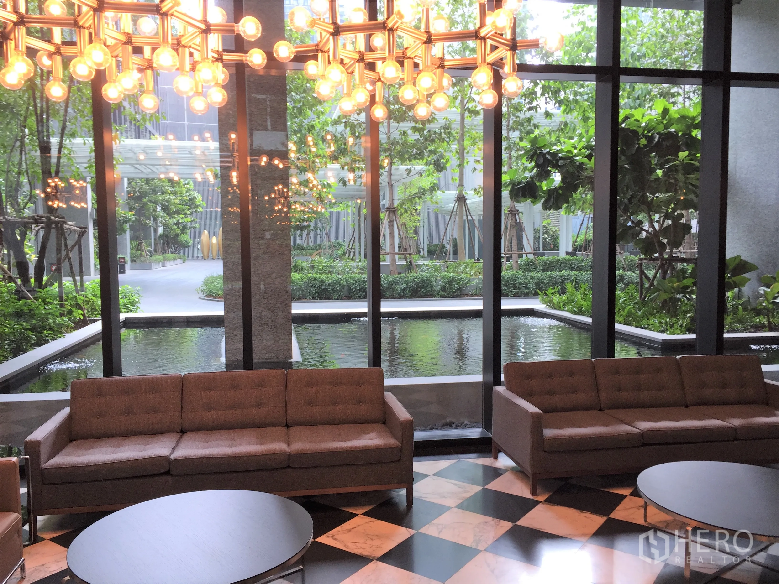 คอนโด ให้เช่าในPathum Wan, Bangkok - ล็อบบี้คอนโดพร้อมโซฟา โคมไฟระย้า และวิวสระน้ำสะท้อนกับสวนสีเขียว