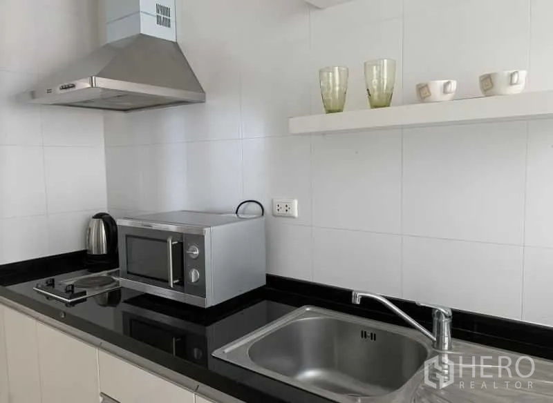 Condominium for rent in Khlong Toei, Bangkok - Modern kitchen with black countertop, sink, microwave, cooktop and range hood.