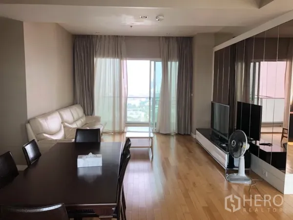 Condominium for rent in Khlong Toei, Bangkok - Bright living and dining area with wood floors, sofa, TV console and balcony city view.