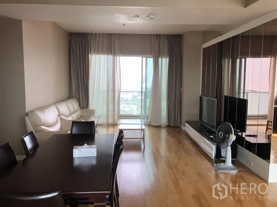 Condominium for rent in Khlong Toei, Bangkok - Bright living and dining area with wood floors, sofa, TV console and balcony city view.
