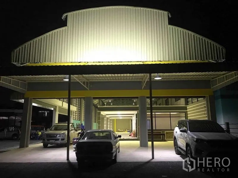 货栈 出租在Bang Pakong, Chachoengsao - 夜间仓库入口雨棚，照明下的停车位与车辆。