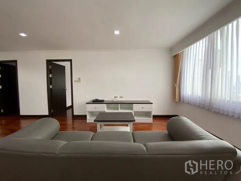 公寓 出租在Watthana, Bangkok - 客厅视角：灰色沙发朝向电视柜，宽幅窗户下的亮泽木地板。