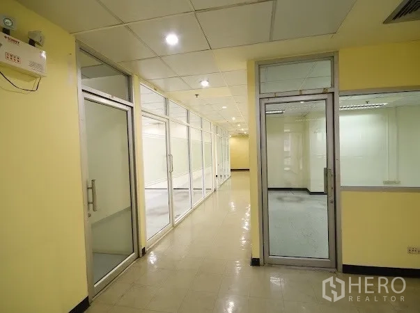 办公空间 出租在Watthana, Bangkok - 明亮走廊，沿线多扇玻璃门通往分隔办公室。