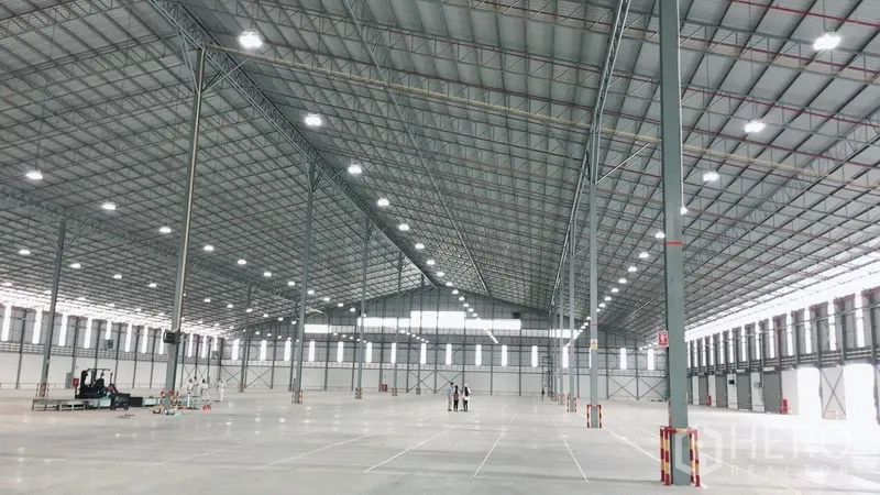 Warehouse for rent in Si Racha, Chon Buri - Expansive high-clearance warehouse interior with steel truss roof, bright LED lighting and polished concrete floor.