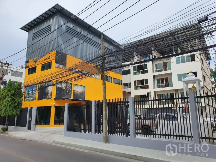 Home Office for rent in Phra Khanong, Bangkok - Streetside view of the gated property featuring a yellow building with a metal roof extension.