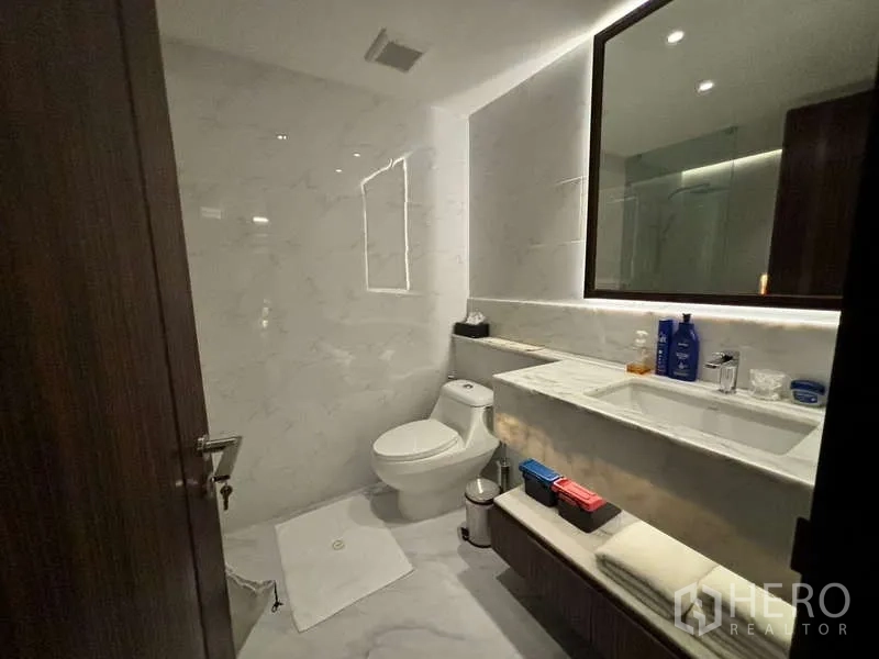 Condominium for rent in Watthana, Bangkok - Modern marble bathroom with backlit mirror, vanity and toilet.