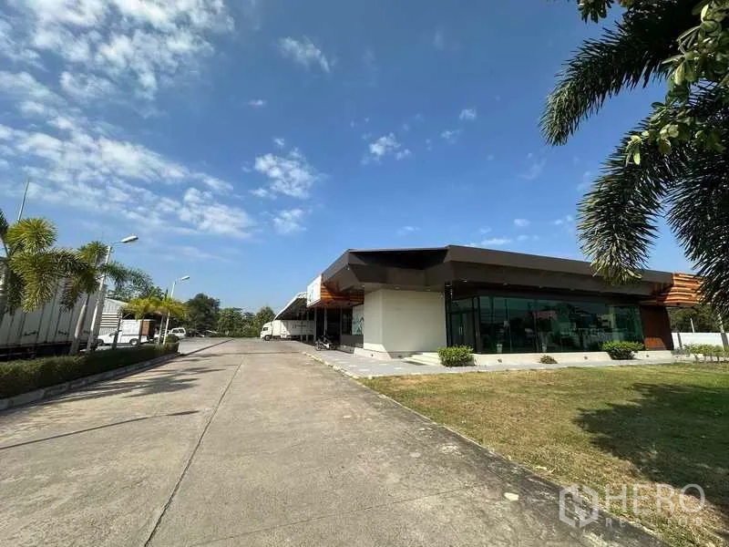 Warehouse for rent in Lam Luk Ka, Pathum Thani - Glass-front office building beside driveway and landscaped lawn at the warehouse complex.