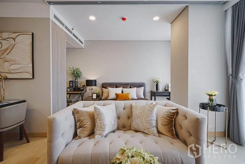Condominium for sale in Khlong Toei, Bangkok - Cozy living zone with cream sofa facing a plush bed, warm lighting and a sliding partition.