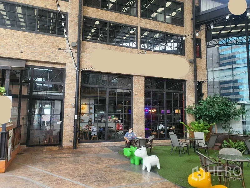 零售空间 出租在Khlong Toei, Bangkok - 砖墙立面与黑框落地窗的店面外观，配户外露台座位、串灯与绿植，澎蓬商圈。
