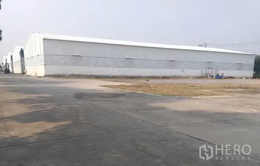 货栈 出租在Pathum Thani - 金属板外墙的仓库外观，前方宽阔混凝土场地