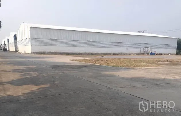 货栈 出租在Pathum Thani - 金属板外墙的仓库外观，前方宽阔混凝土场地