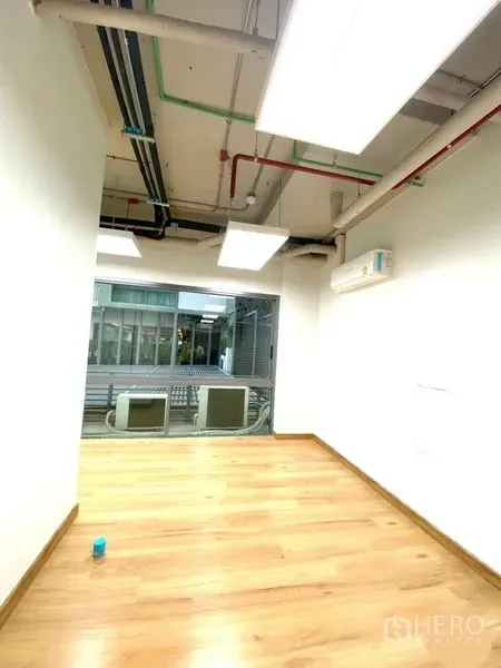 Office Space for rent in Khlong Toei, Bangkok - Bright narrow office with wood flooring, white walls, exposed ceiling pipes, window and wall AC.