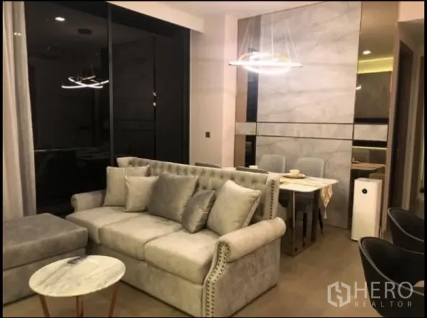 公寓 出租在Watthana, Bangkok - 客厅配灰色沙发、仿石纹背景墙与落地窗。
