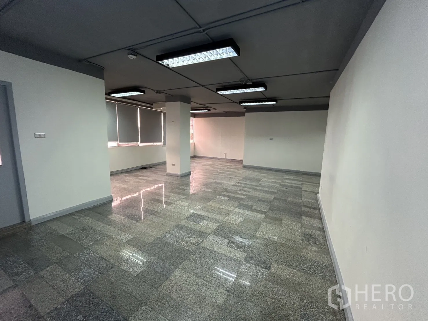 Office Space for rent in Khlong Toei, Bangkok - Open-plan office with polished stone tile floors, columns, roller blinds, and fluorescent ceiling lights.