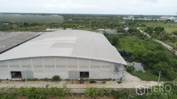 โรงงาน ให้เช่าหรือขายในKrathum Baen, Samut Sakhon - ภาพโดรนแสดงอาคารคลังสินค้าโครงหลังคาชิ้นเดียว ถนนทางเข้าและบ่อใกล้พื้นที่สีเขียว