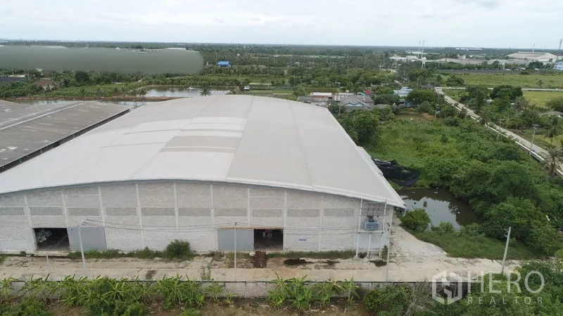 โรงงาน ให้เช่าหรือขายในKrathum Baen, Samut Sakhon - ภาพโดรนแสดงอาคารคลังสินค้าโครงหลังคาชิ้นเดียว ถนนทางเข้าและบ่อใกล้พื้นที่สีเขียว