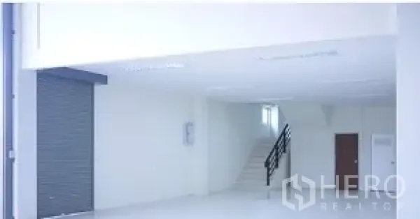 Factory for rent in Mueang Samut Sakhon, Samut Sakhon - Clean loading area with roller shutter, bright white interior and staircase leading to a mezzanine platform.