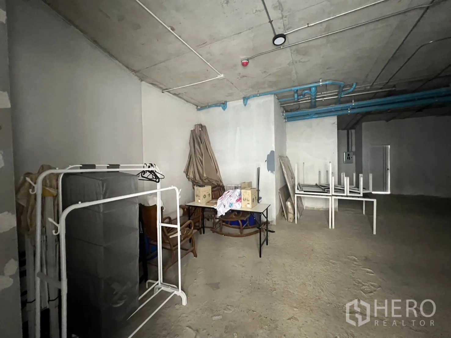 Retail Space for rent - Storage corner inside the unit with racks, stacked tables and exposed services.