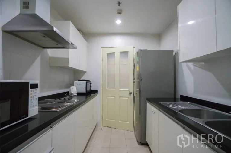 Condominium for rent or sale in Khlong Toei, Bangkok - Closed galley kitchen with white cabinets, black countertops and appliances.