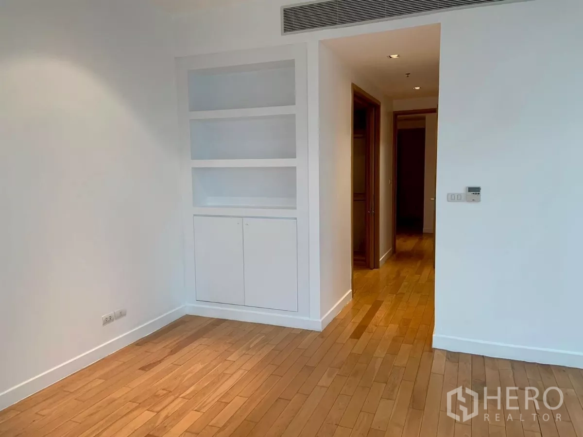 Condominium for rent in Khlong Toei, Bangkok - Bedroom with built-in shelves and cabinet, white walls and timber floor.