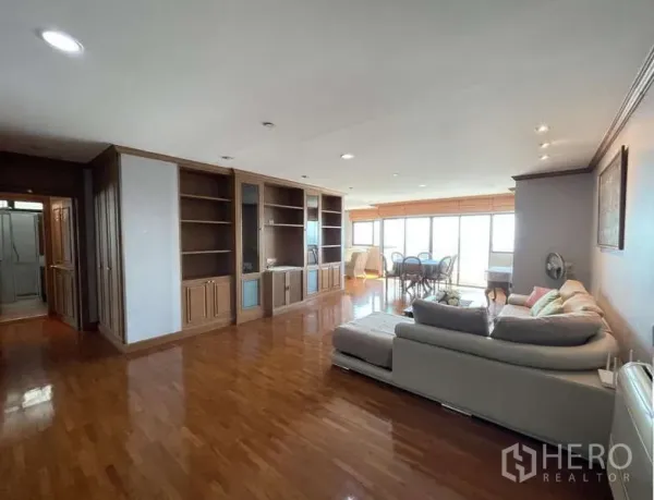 Condominium for rent - Wide living room with glossy wood floors, built-in shelving and dining area by windows.